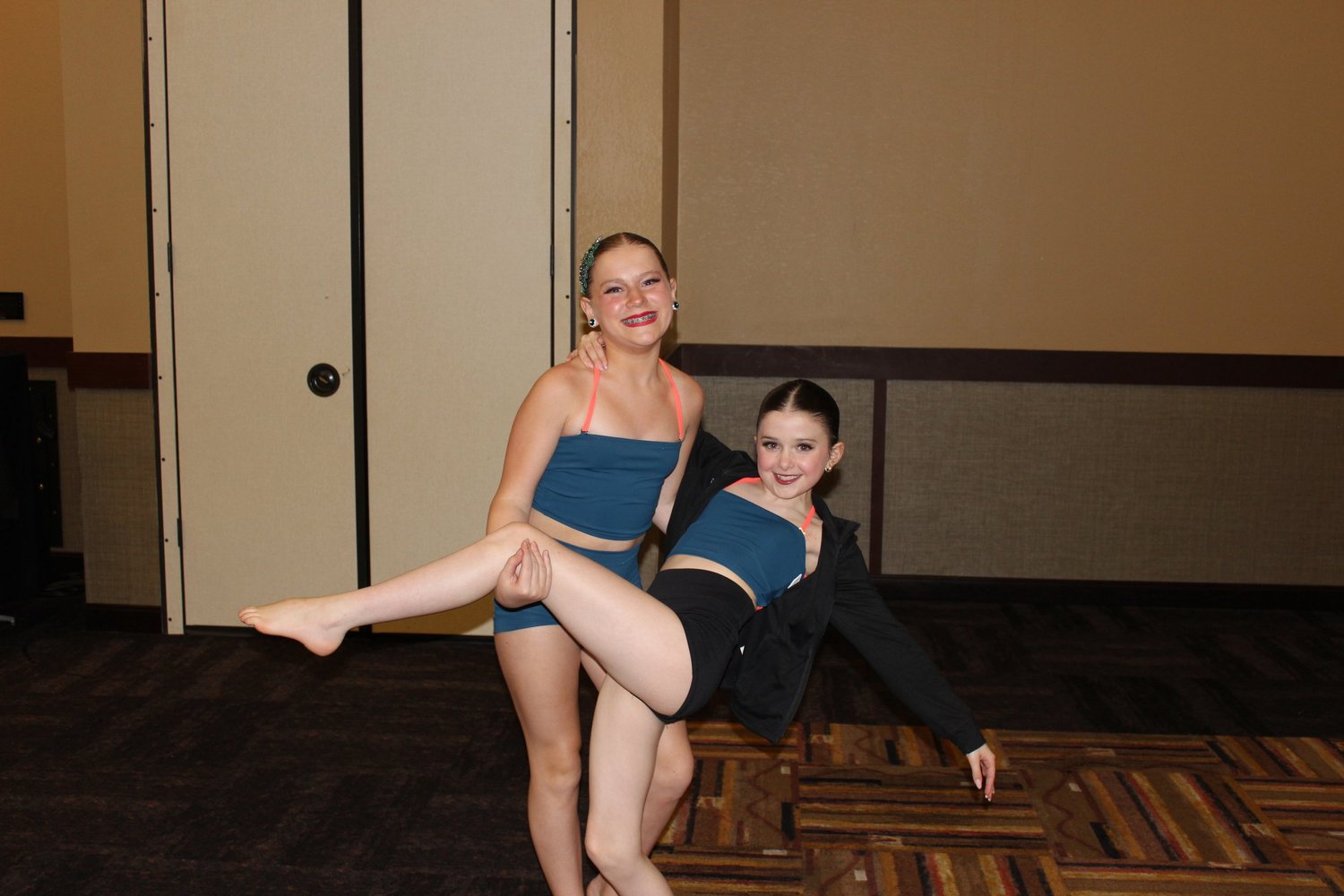 Two dancers in matching blue costumes sharing a playful dance pose.