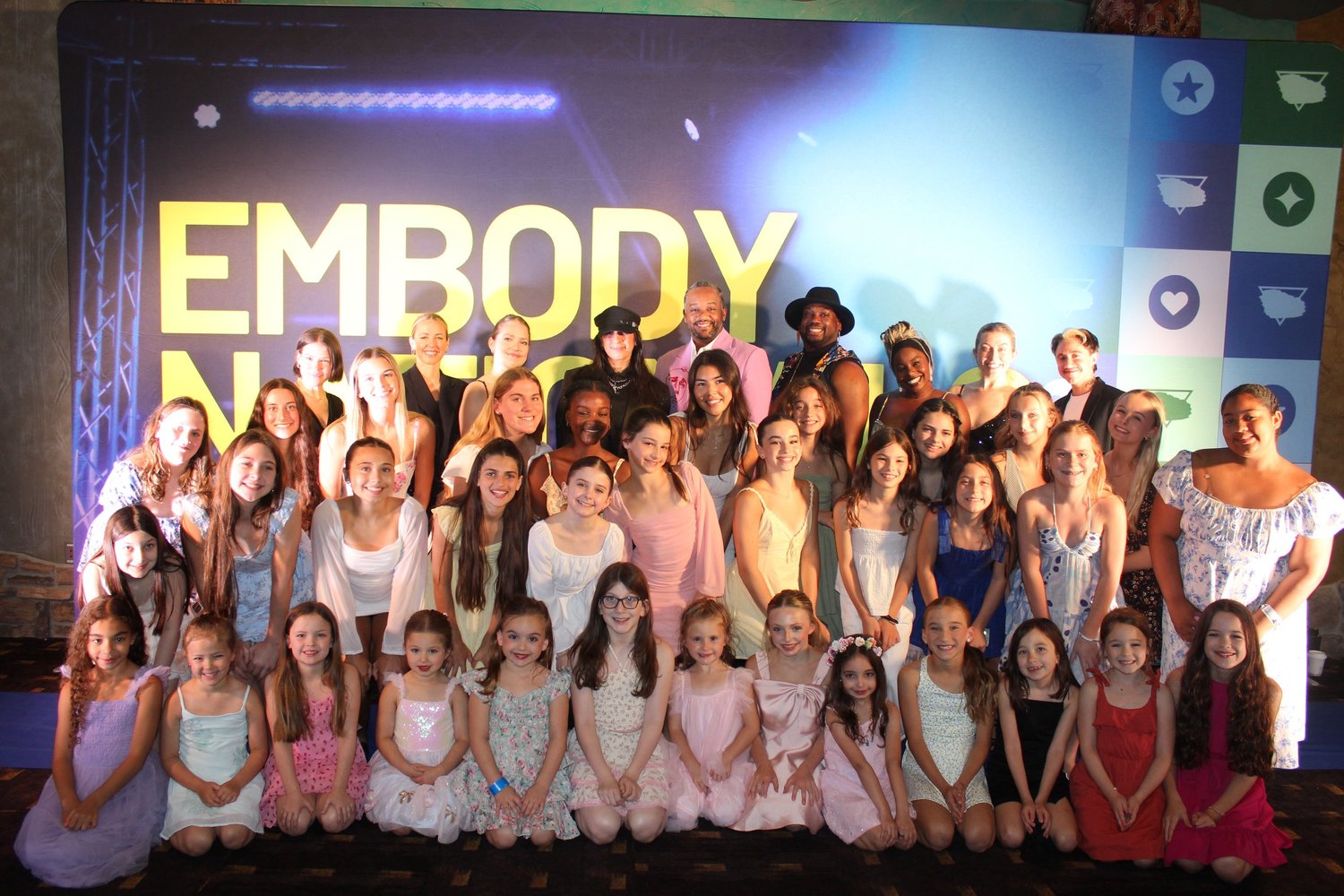 Dancers and adults gathered for a group photograph in front of the Embody backdrop.